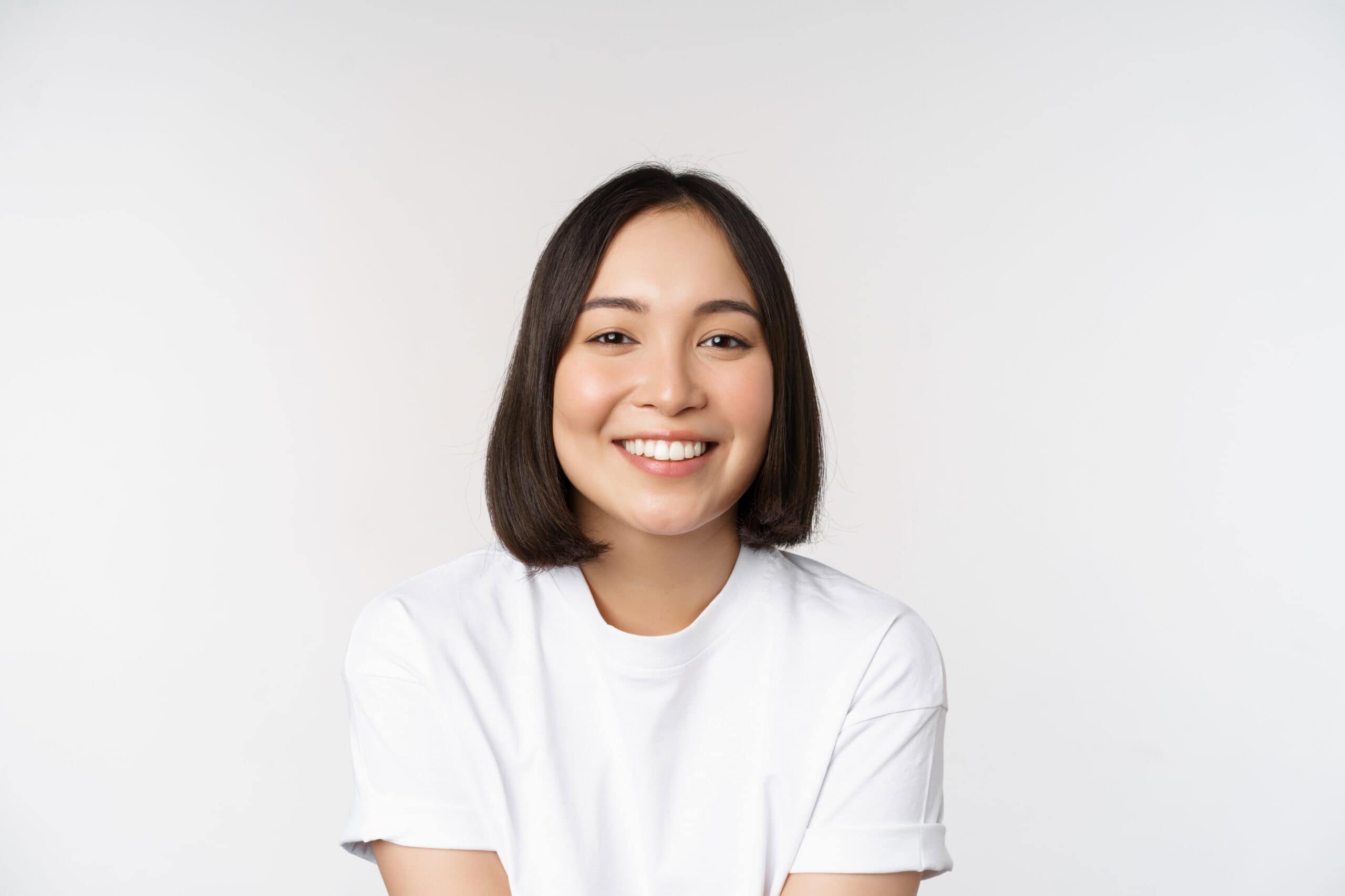 Beautiful korean girl smiling, white teeth, looking lovely at camera, standing in white tshirt over studio background